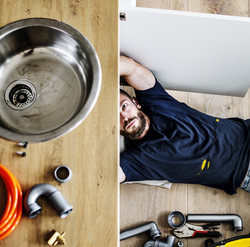 man fixing pipes under kitchen sink